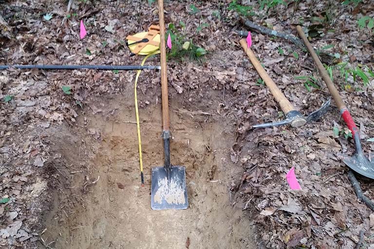 Soil pit at Lilly-Dickey Woods. Shovels and a pick are on the ground by the pit.