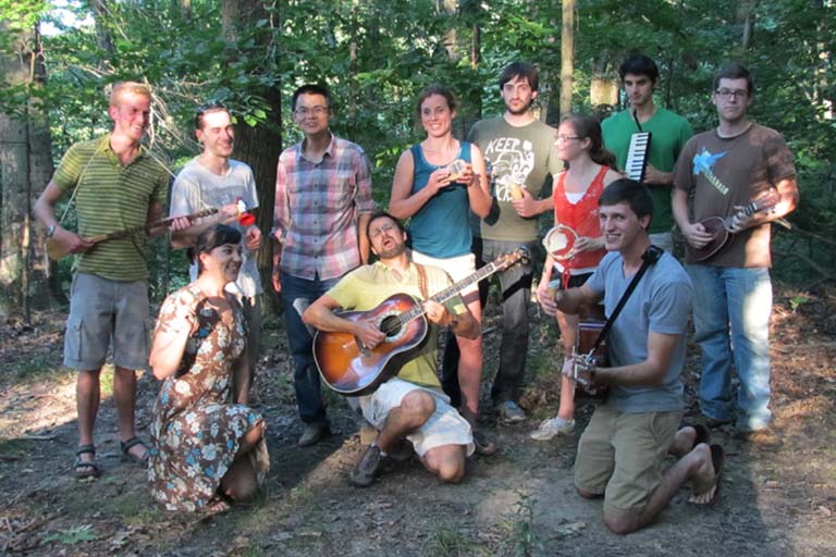Lab members gather for a group photo in the woods with guitars and other musical instruments.