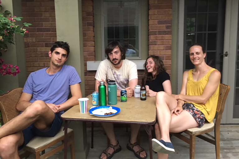 Four lab members enjoy some social time around a table on a porch after lunch.